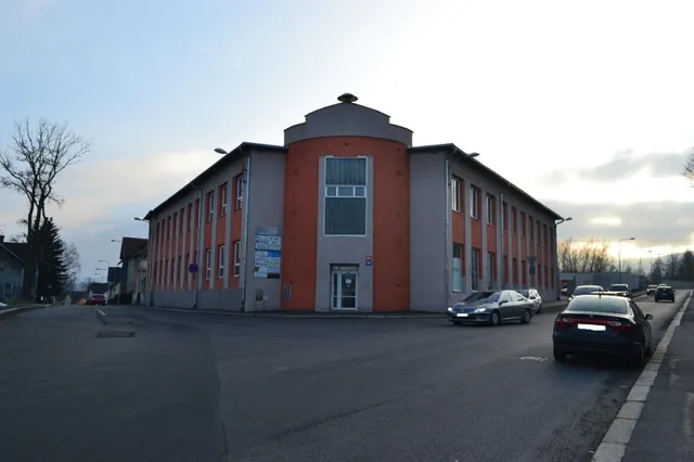 Budova s provozovnou autoservisu z ulice za soumraku, před ní parkující osobní vozy