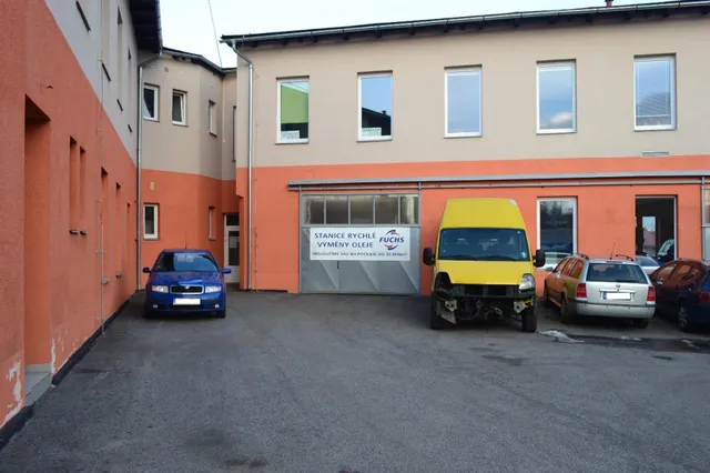 Vjezd do servisu s otevřenou dílenskou halou a odstavenými vozy na dvoře